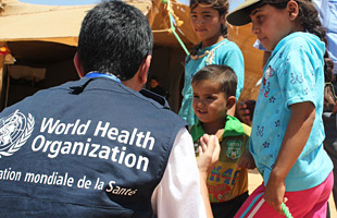 A WHO field worker talks to refugee childen at a camp in Jordan.